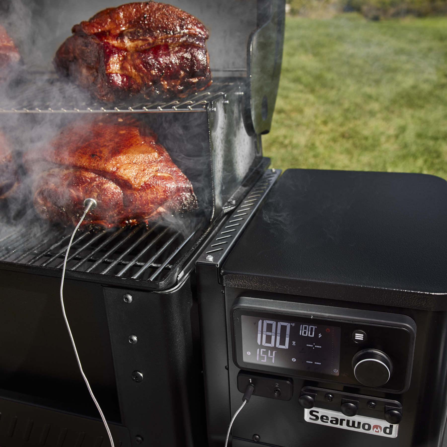 Weber Searwood pellet hopper open with hardwood pellets visible — the auger feeds pellets from the hopper into the burn pot where the hot rod ignites them.
