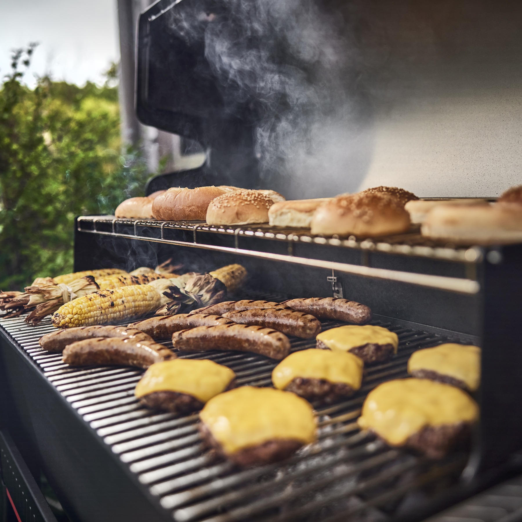 Burgers with cheese, bratwurst, grilled corn, and buns toasting on the Searwood's grate — pellet smokers also grill at 500°F plus.